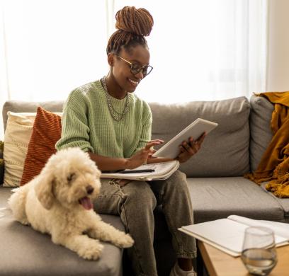 Woman sitting with her dog on a sofa using a tablet