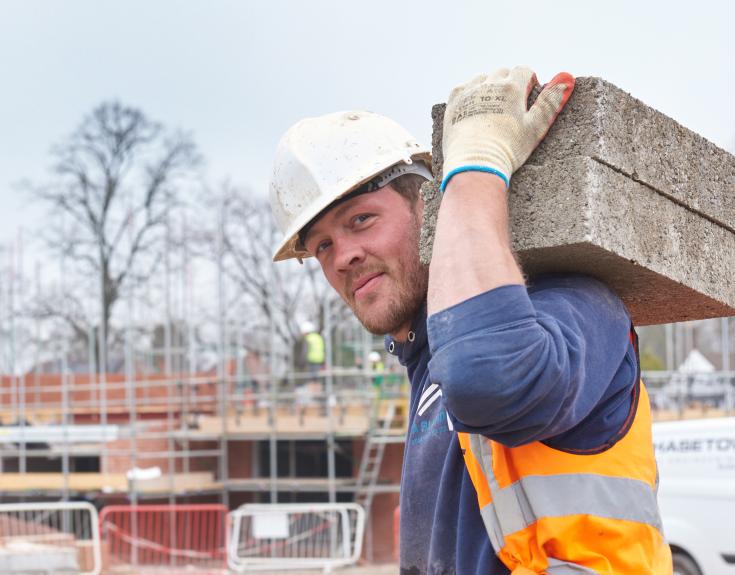 Builder carrying bricks wearing hard hat Cameron development