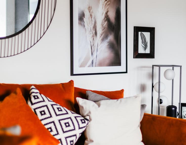 Orange couch against white wall with picture frames and mirror